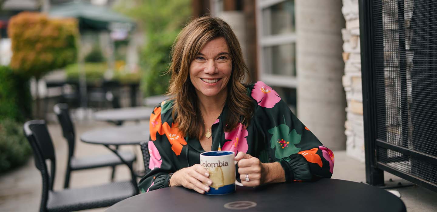 Smiling woman in flowered shirt holding mug that says "Colombia"